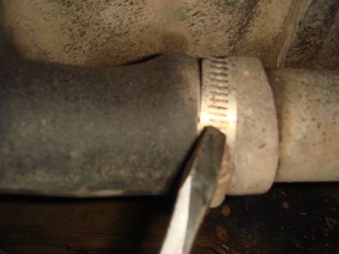1996 Ford Bronco - Close-up of a worm-gear hose clamp secured around a rubber boot or hose connecting to a metal pipe, with a flathead screwdriver tip positio…