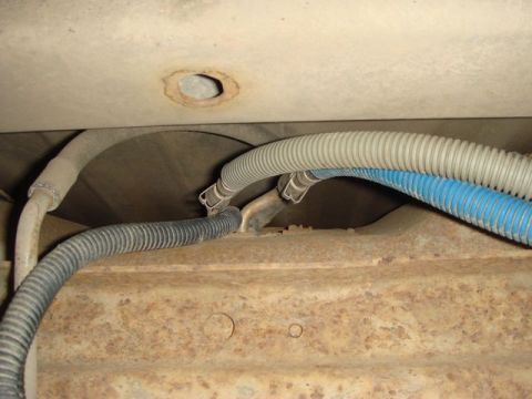 1996 Ford Bronco - Underbody view showing corrugated conduit and hoses, including a blue-striped flex line and gray convoluted tubing, routed near a rusty fra…