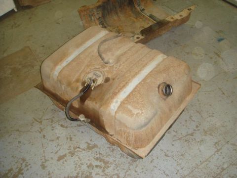 1996 Ford Bronco - A rusty, tan-colored automotive fuel tank sitting on a cardboard sheet on a concrete floor, with the sending unit and fuel line hose visibl…