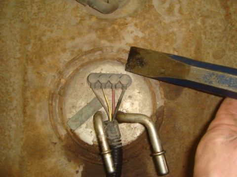 1996 Ford Bronco - Close-up of a fuel pump/sending unit assembly atop a rusty fuel tank, showing a gray multi-pin electrical connector with colored wires and…