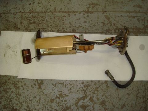 1996 Ford Bronco - A fuel pump sending unit assembly removed from a fuel tank, laid on white paper over a concrete floor, showing the tan/gold reservoir housi…