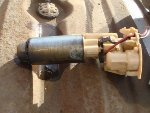 1996 Ford Bronco - A used electric fuel pump assembly with a metallic cylindrical motor body and tan/beige plastic housing, showing red and black wiring conne…