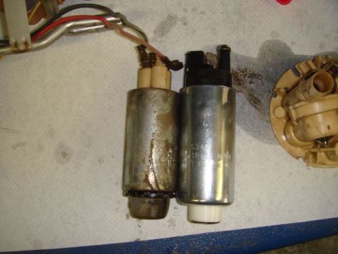 1996 Ford Bronco - Two cylindrical automotive fuel pumps laid side by side on a paper towel over a blue surface; the left pump is corroded and dirty while the…
