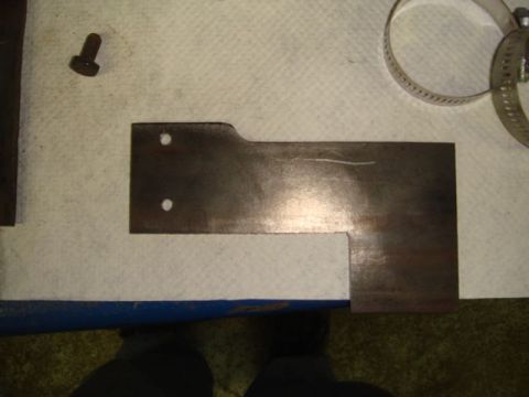 1996 Ford Bronco - A flat steel bracket or mounting plate with an L-shaped cutout and two drilled holes rests on a padded workbench, alongside a hex-head bolt…