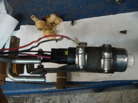 1996 Ford Bronco - A disassembled fuel pump/sending unit assembly laid on a white shop towel over a blue work surface, showing the pump motor, wiring harness…
