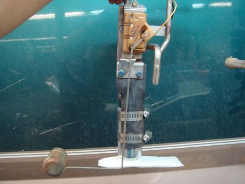 1996 Ford Bronco - Close-up of a fuel pump assembly or sending unit being serviced on a workbench, showing the top-mounted electrical connector, mounting brac…