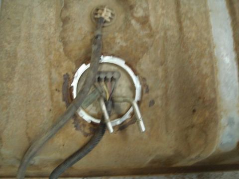 1996 Ford Bronco - Close-up of a rusty fuel tank showing the fuel pump/sending unit lock ring with the connector and wiring harness partially disconnected. Th…