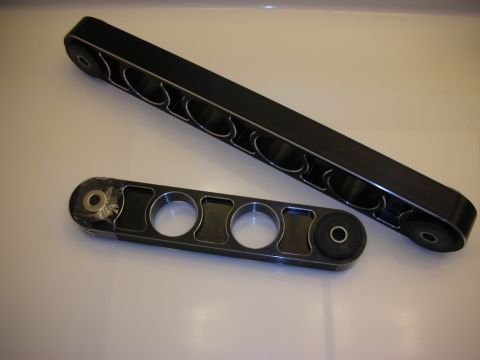 1998 Ford Crown Victoria - Two black aftermarket control arms, one longer than the other, are displayed on a white surface. They feature a series of circular cutouts…