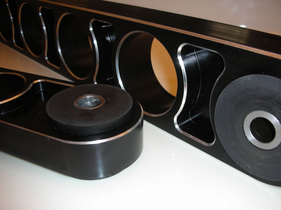 Black aluminum control arms with rubber bushings on a tan surface