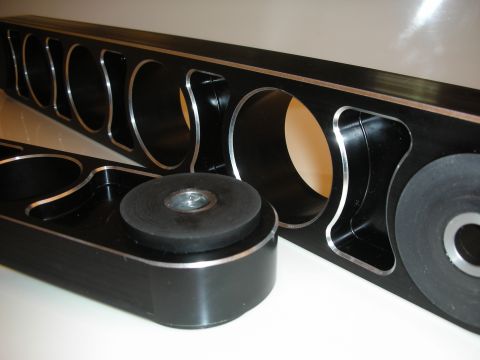 1998 Ford Crown Victoria - Two black metal control arms with circular cutouts and rubber bushings are shown in a close-up view.