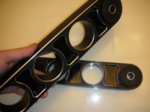 1998 Ford Crown Victoria - A hand holds a pair of aftermarket control arms, a black finish with polished edges and large circular cutouts.