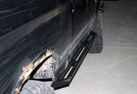 1994 Ford Bronco - Aftermarket rock sliders installed on a black SUV, showing side profile and some rust damage.