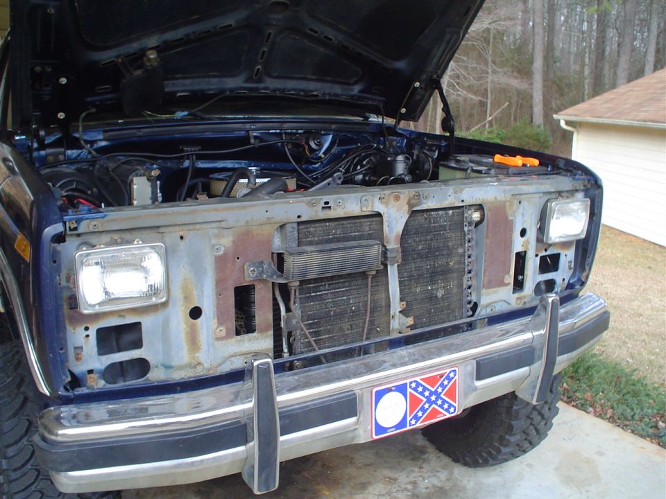 Front view of a blue Ford truck, hood open, showing engine bay and radiator. Rebel flag sticker on bumper