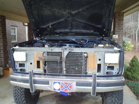 1984 Ford Bronco - Front view of a blue SUV, hood open, revealing the engine compartment and grille, with a decorative plate on the bumper.