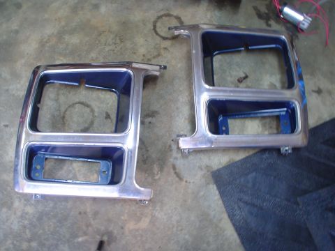 1984 Ford Bronco - A pair of chrome headlight bezels are shown on a concrete floor, ready for installation or repair.