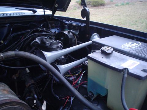 1984 Ford Bronco - Engine bay of a 1984 Ford Bronco, dual air horns and visible Ford branding on the engine cover.