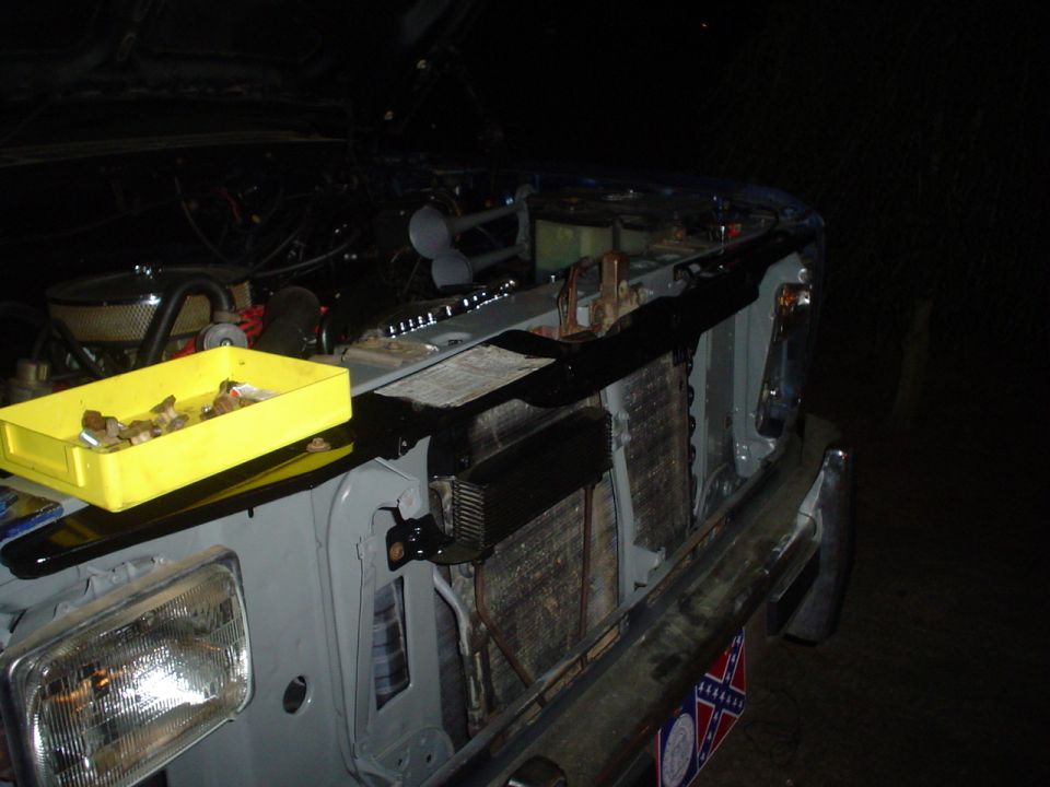 Vehicle front end with hood open, showing engine bay, radiator, and a yellow parts tray
