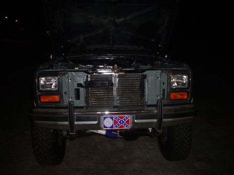 1984 Ford Bronco - The front grille and headlights of a Ford truck are visible with the hood open at night.