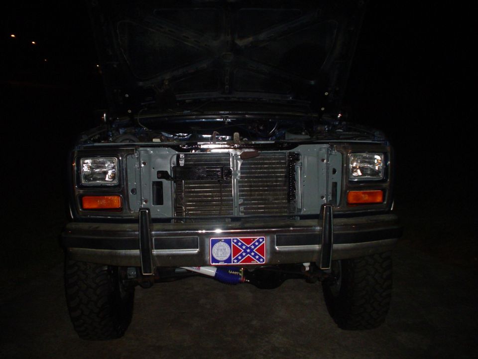 Front of a Ford truck with hood open. Has a confederate flag license plate frame