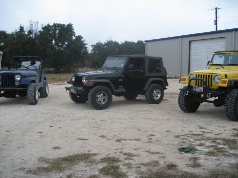 2001 Jeep Wrangler - Three Jeep Wranglers are parked in a gravel lot in front of a large building.