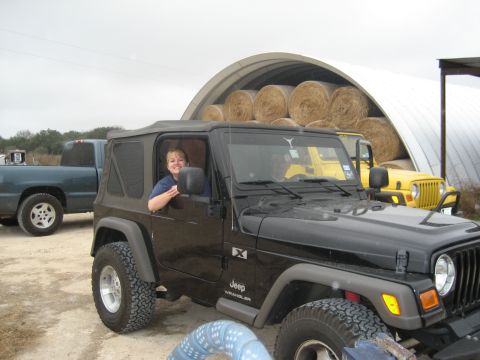 2001 Jeep Wrangler - A black Jeep Wrangler is parked outdoors with a woman in the driver's seat, alongside other vehicles and hay bales.