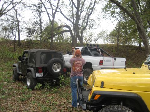 2001 Jeep Wrangler - A black 2001 Jeep Wrangler is parked off-road, viewed from the rear, with other vehicles nearby.