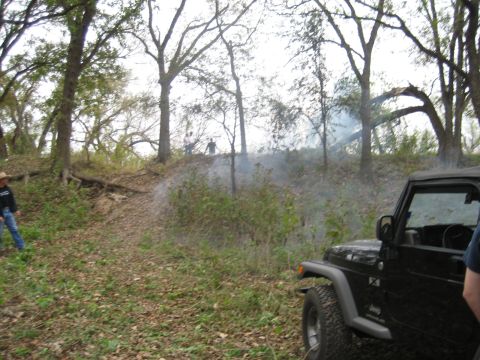 2001 Jeep Wrangler - A black Jeep Wrangler is parked on a dirt path in a wooded area, with smoke rising in the distance.