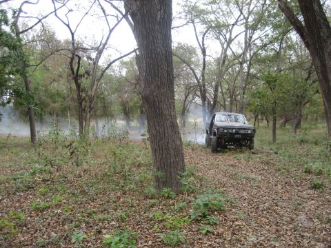 2001 Jeep Wrangler - A truck drives through a wooded area, emitting smoke from its exhaust.