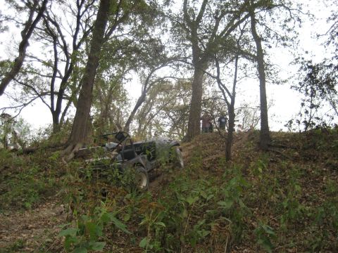 2001 Jeep Wrangler - An off-road vehicle is parked on a steep, wooded incline with several people visible on the ridge above.