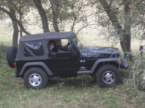 2001 Jeep Wrangler - A black 2001 Jeep Wrangler is seen from the side, driving through a wooded area with two people inside.