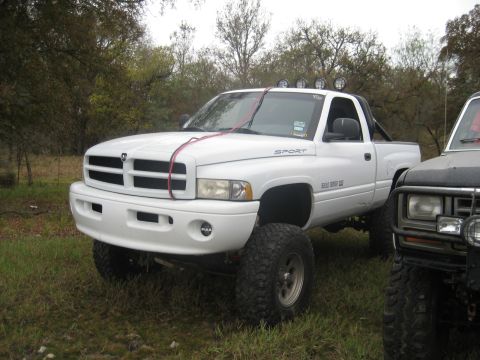 2001 Jeep Wrangler - A lifted white Dodge Ram pickup truck is parked outdoors next to another vehicle.