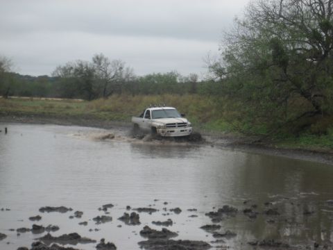 2001 Jeep Wrangler - A white pickup truck navigates through a muddy, water-filled area, kicking up spray.