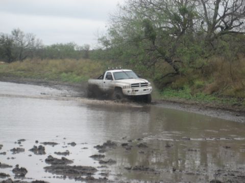 2001 Jeep Wrangler - A white pickup truck navigates a muddy, water-filled path, kicking up spray as it goes.