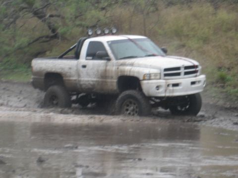 2001 Jeep Wrangler - Modified Dodge Ram pickup truck navigating a muddy off-road course.
