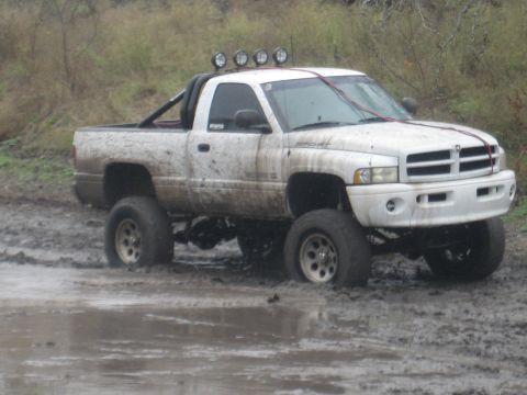 2001 Jeep Wrangler - A white Dodge Ram pickup truck is stuck in deep mud, with its tires partially submerged.