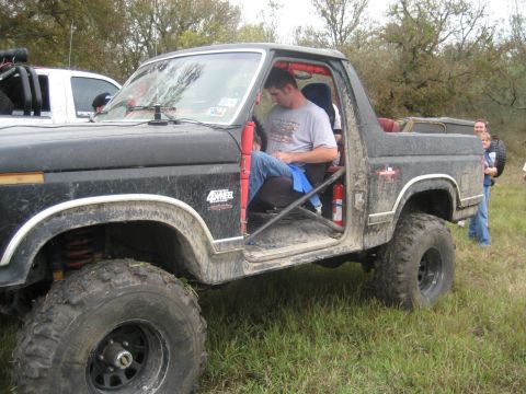 2001 Jeep Wrangler - Modified black pickup truck with roll cage parked in a grassy field, another vehicle behind.