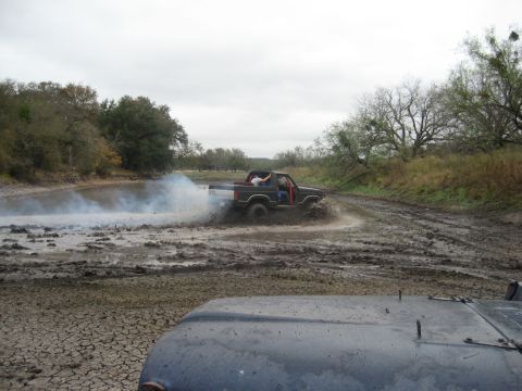 2001 Jeep Wrangler - A truck navigates a challenging muddy terrain, creating a plume of smoke and splashing water.