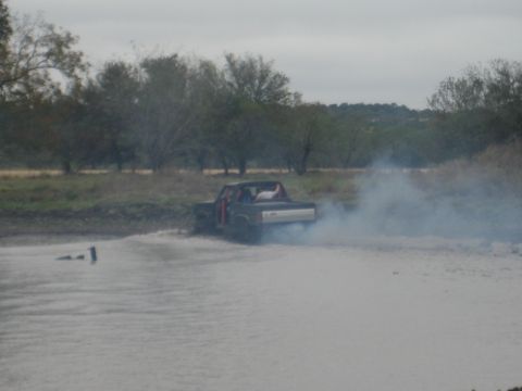 2001 Jeep Wrangler - A pickup truck kicks up mud and smoke as it spins its tires in a muddy area.