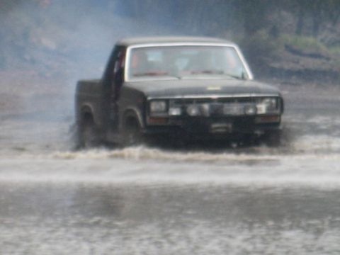 2001 Jeep Wrangler - A black pickup truck navigates through murky water, kicking up spray.