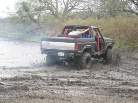 2001 Jeep Wrangler - This Ford Bronco is navigating a muddy terrain, with its tires splashing through the muck.