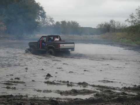 2001 Jeep Wrangler - A brown pickup truck navigates through a muddy area, kicking up water and dirt.