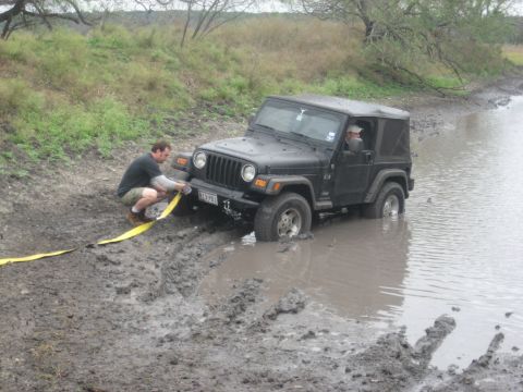 2001 Jeep Wrangler - A person is attaching a tow strap to a black Jeep Wrangler that is stuck in muddy water.