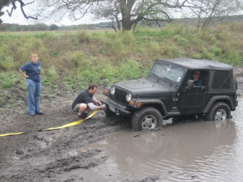 2001 Jeep Wrangler - A Jeep Wrangler is stuck in a muddy puddle while two people attempt to free it with a tow strap.