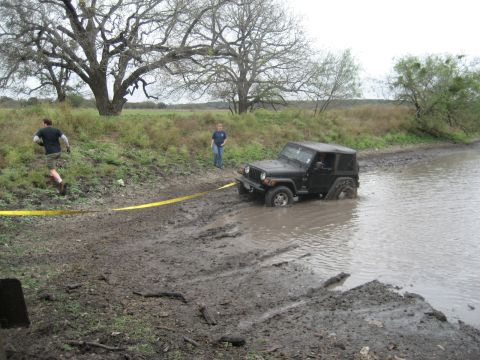 2001 Jeep Wrangler - A black 2001 Jeep Wrangler is stuck in a muddy, watery ditch, with two people nearby.