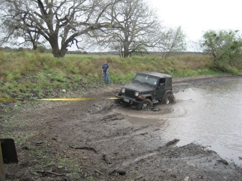 2001 Jeep Wrangler - A black Jeep Wrangler is stuck in the mud near a body of water, with a person standing nearby.