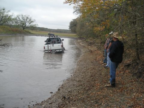 2001 Jeep Wrangler - A white pickup truck navigates through a shallow body of water, observed by onlookers on the muddy shore.