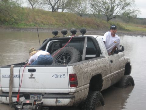 2001 Jeep Wrangler - A white Dodge 4x4 pickup truck is stuck in muddy water with two people inside.