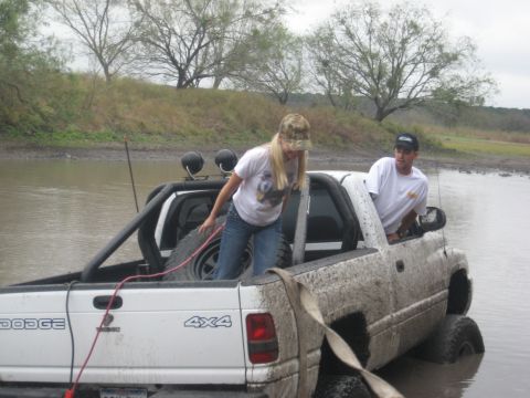 2001 Jeep Wrangler - Two people in a white Dodge pickup truck that is stuck in muddy water.