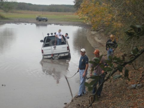 2001 Jeep Wrangler - A white pickup truck is stuck in a body of water with people observing from the bank.