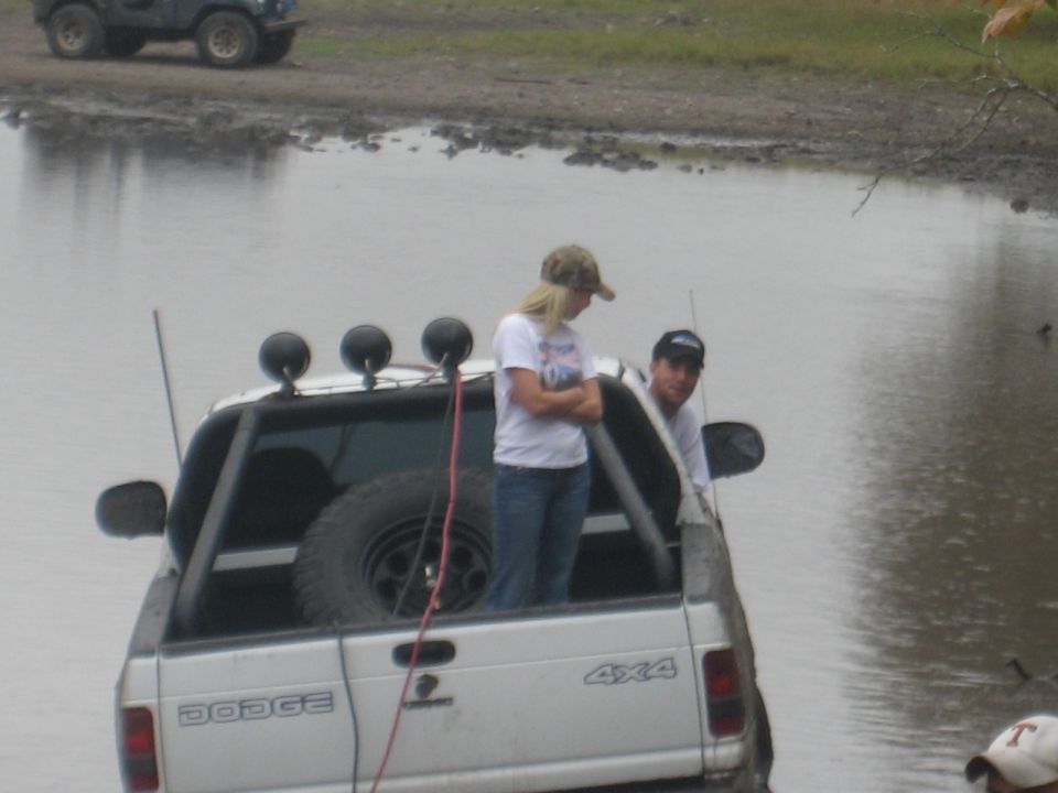 White Dodge pickup truck with 4x4 badging stuck in water, people in bed